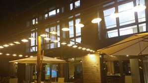 An outdoor dining area with multiple tables and chairs, large umbrellas, and hanging lights.