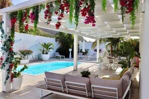 Ein Poolbereich mit weißer Pergola, Sitzgelegenheiten im Freien und Topfpflanzen.