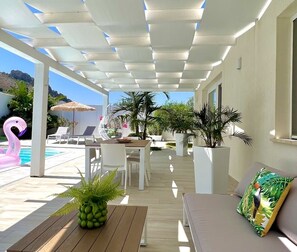 Ein überdachter Außenbereich mit Pool, Liegestühlen und einem Esstisch mit Pflanze.
