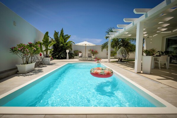 Ein Schwimmbecken mit einem schwimmenden Ring, umgeben von Kübelpflanzen und Gartenmöbeln.