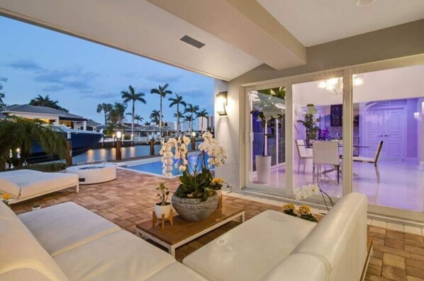 Relax in a spacious room with a sliding glass door leading to an outdoor area, featuring a comfortable seating area and a large window with a view of the pool and palm trees.