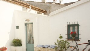 Une rue étroite avec un bâtiment blanc, une porte verte, un banc en pierre, des plantes en pot et un vélo.