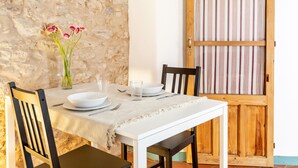 Une table à manger dressée avec de l’assiette, des bols et des verres blancs, un vase rempli de fleurs roses et une chaise en bois.