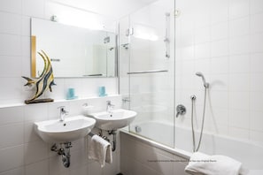 Un baño moderno con dos lavamanos, ducha con cerramiento de vidrio y bañera.