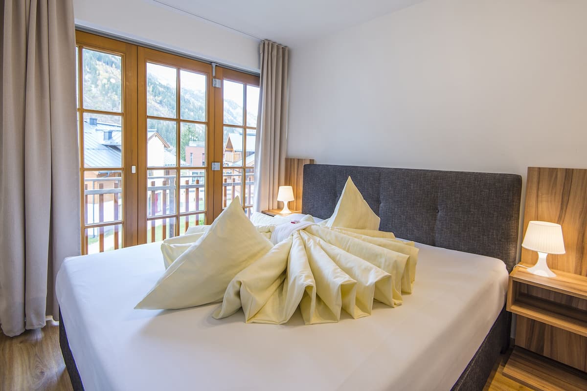 A neatly made bed with a large, decorative pillow arrangement, a wooden headboard, and a nightstand with a lamp.