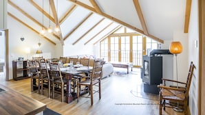 Een ruime eetruimte met houten stoelen en een grote tafel, een gezellige zithoek met een bank, en een open haard.