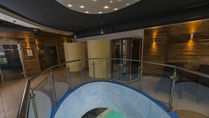 Een gebogen glazen balustrade, een vloer in blauw en groen, houten paneelwanden en een plafond met inbouwverlichting.