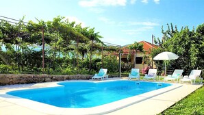 A swimming pool with lounge chairs and umbrellas, surrounded by greenery and a stone wall. - Sunflower House With a Pool and Large Garden (Omis)
