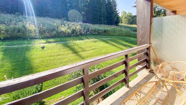 Un balcon en bois donnant sur un champ verdoyant et des arbres.