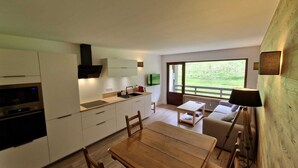Une cuisine moderne dotée d’appareils électroménagers intégrés, un coin repas avec une table et des chaises en bois, et une grande fenêtre offrant une vue sur l’extérieur.