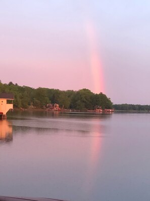 A calm lake with a rainbow, buildings on the shore, and trees in the background. - Hidden Cove (Findley Lake)