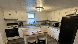 A compact kitchen with white cabinets, a wooden island with two stools, a black refrigerator, and a microwave. - Peaceful Single-Level Retreat, Near Harpers Ferry,  Easy Access + Prime Location (Harpers Ferry)