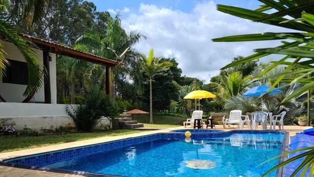 Una piscina rectangular con azulejos azules, rodeada por una solana también con azulejos. Se observan sillas reclinables blancas y un paraguas amarillo.