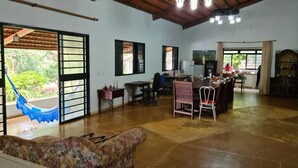 Amplia sala de estar con techo alto, una hamaca, una mesa de comedor con sillas y una zona de cocina.