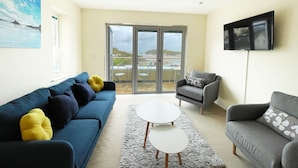 A living room with a blue sofa, a grey sofa, a white coffee table, and a grey armchair. There is a large window with a view of the outdoors.