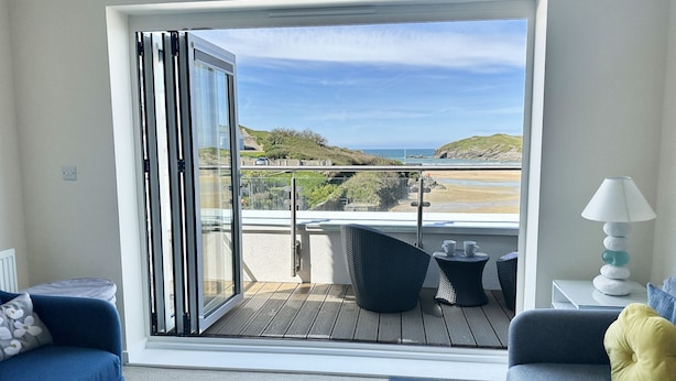 A balcony with a view of the beach, a sofa, a table with a lamp, and a chair.