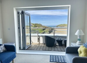 Un balcón con vistas a la playa, un sofá, una mesa con una lámpara y una silla.