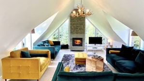 A spacious loft with a stone fireplace, a large TV, and a unique chandelier. - Muir Estate (Stirling)