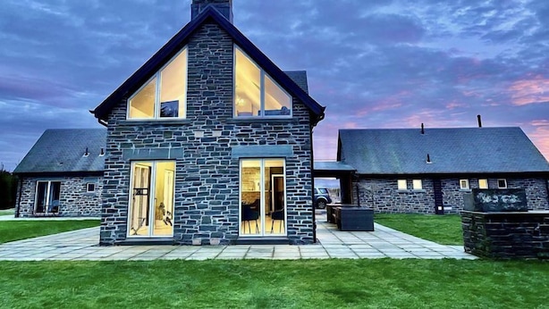 A modern stone house with a large glass front and a chimney. - Muir Estate (Stirling)