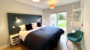 A bedroom with a large bed, a nightstand, a green chair, and a sliding glass door to the outside. - Muir Estate (Stirling)