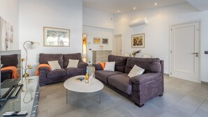 Een moderne woonkamer met twee grijze banken, een glazen salontafel en een flatscreen televisie.