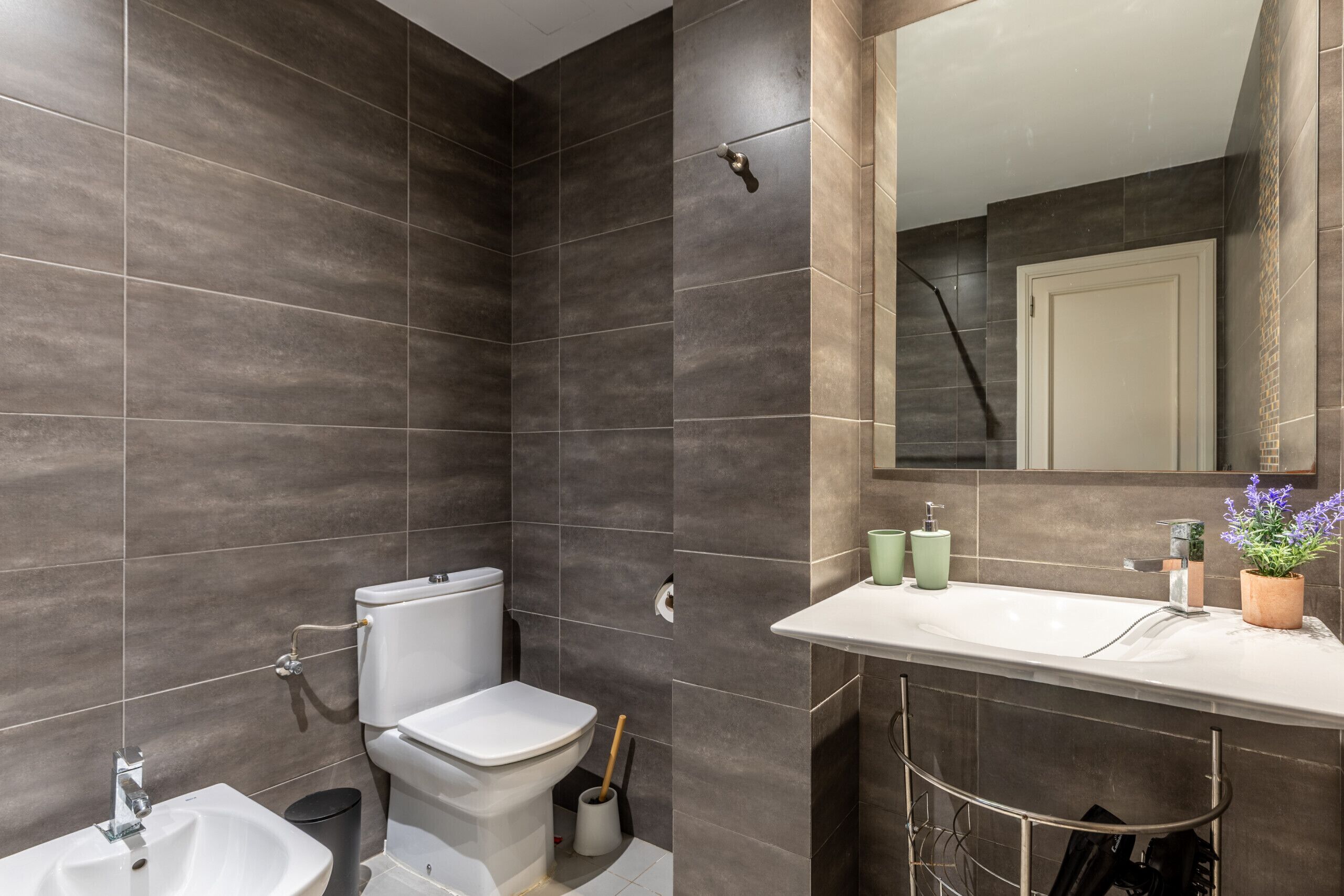 A bathroom with dark tiles, a toilet, a sink, and a mirror.