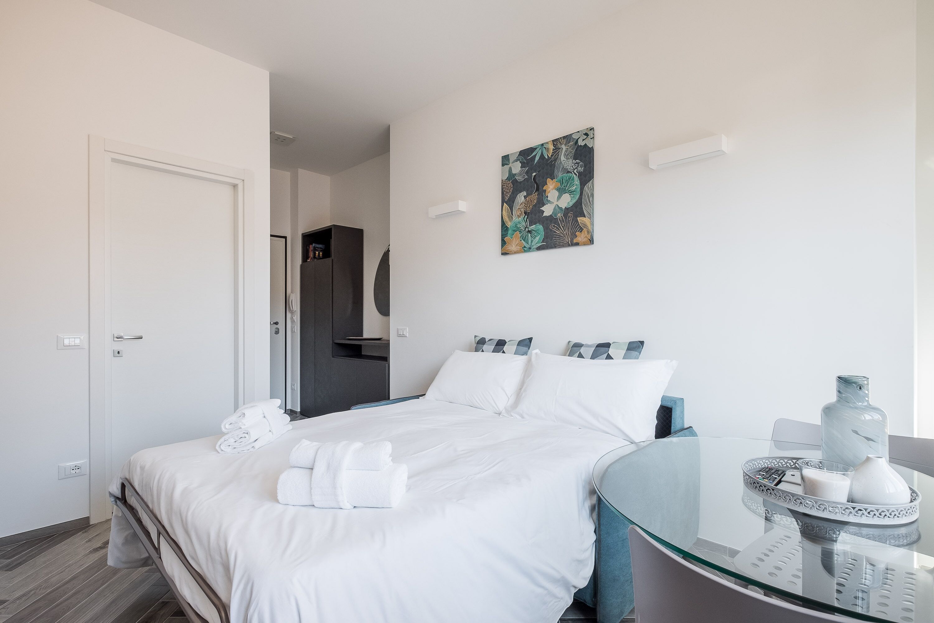 Une chambre d’hôtel avec un lit, une table en verre sur laquelle se trouve un plateau, et un tableau accroché au mur.