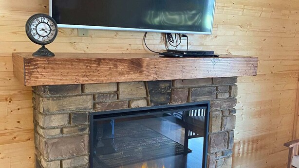 A stone fireplace with a TV mounted above it, a clock on the mantel, and a fire burning inside. - Cabin Sleeps 12, Hot Tub, Movie Room, Game Room (Sevierville)