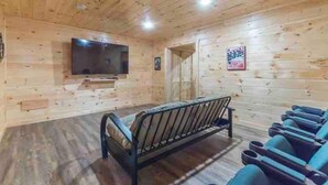 A wooden cabin interior with a bed, a bench, and a TV mounted on the wall. - Cabin Sleeps 12, Hot Tub, Movie Room, Game Room (Sevierville)