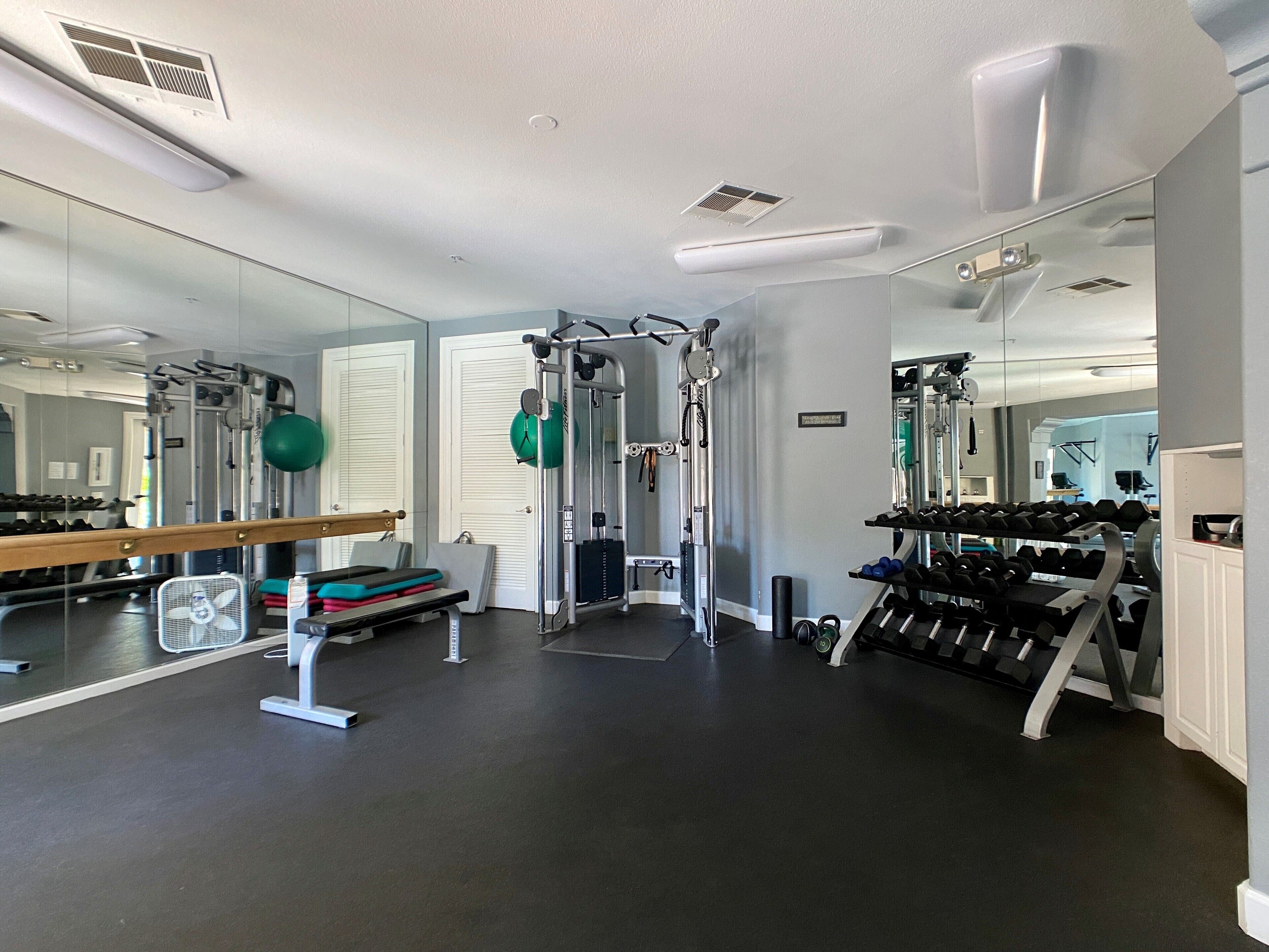 A gym with exercise equipment, mirrors, and a rack of dumbbells.