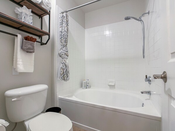 Un baño moderno con inodoro blanco, bañera, ducha y un estante con toallas y artículos de aseo.