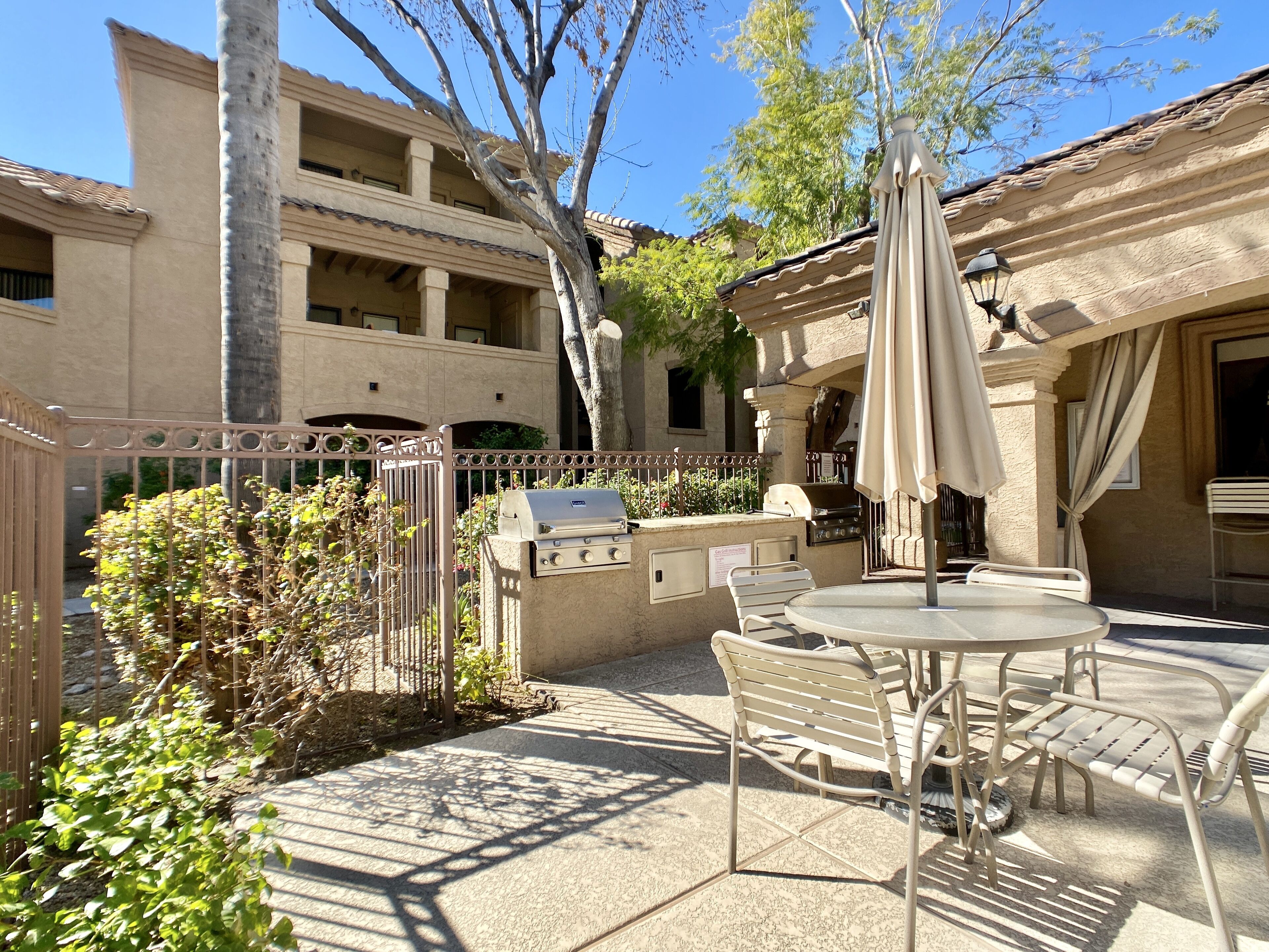 An outdoor patio with a grill, table, and chairs.