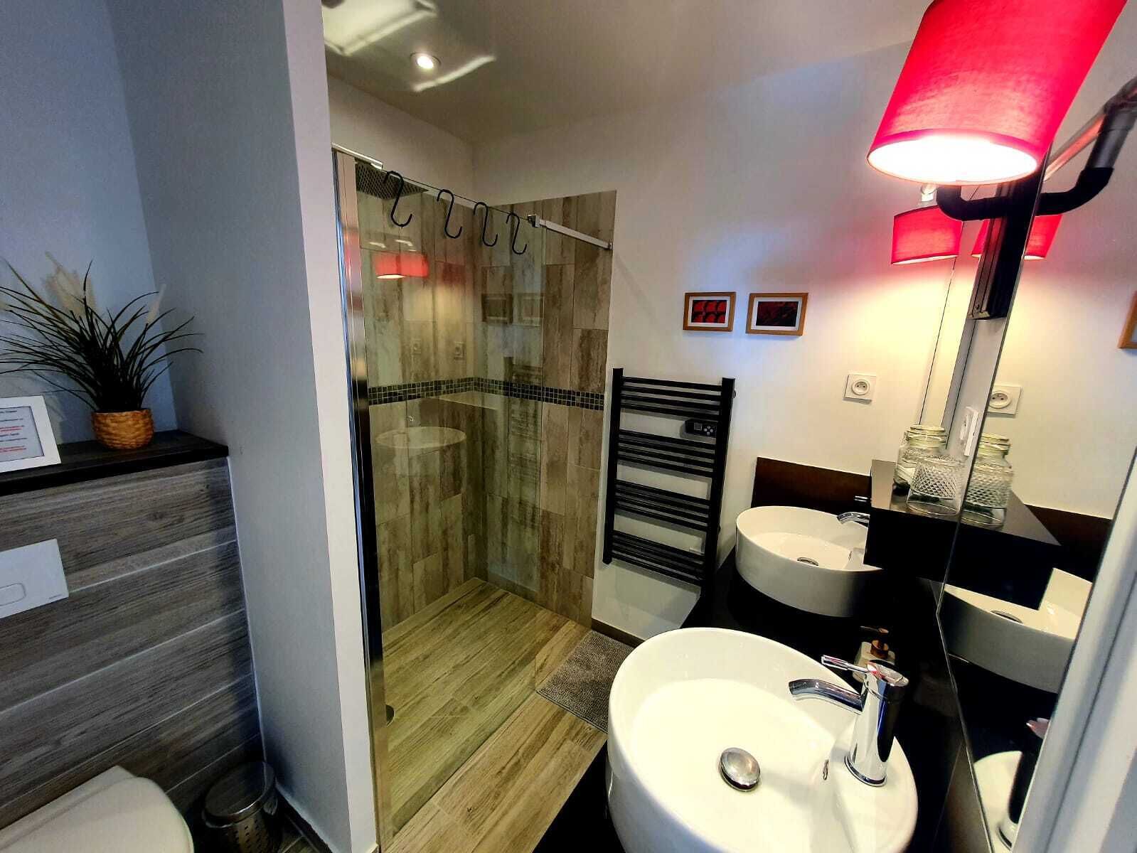 Un baño moderno con cabina de ducha de vidrio, tocador de madera y un espejo grande con luz roja.