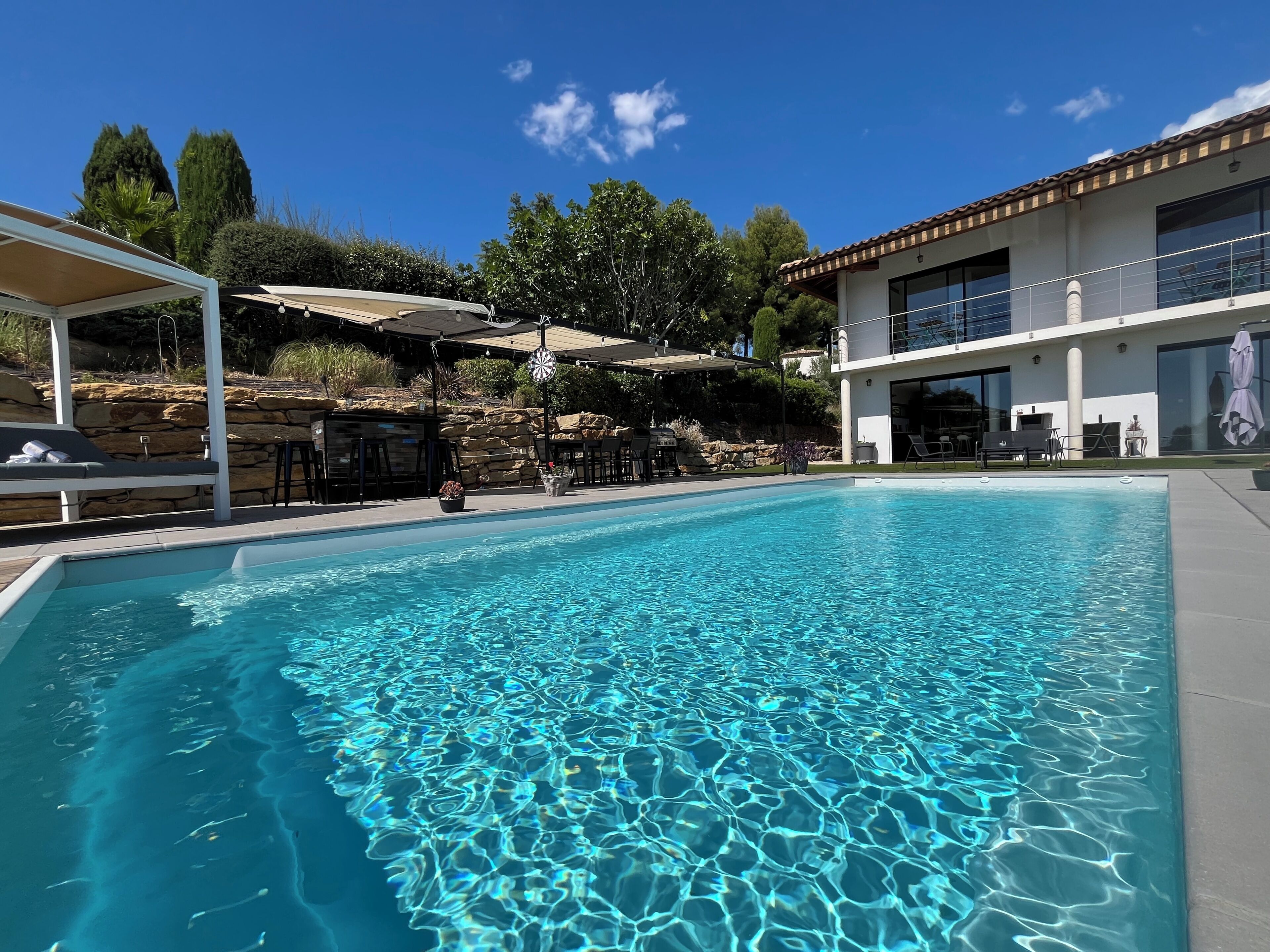 A clear swimming pool with a stone wall and outdoor seating area.