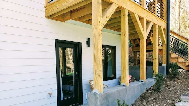 Ein modernes Haus mit einer Holzterrasse, einem Betonpflanzgefäß und einer schwarzen Tür.