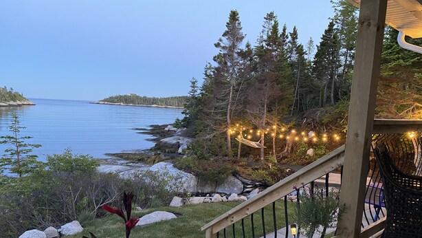 Une terrasse en bois dotée d’une balustrade, qui offre une vue sur une étendue d’eau, le tout entouré d’arbres et bordé d’une côte rocheuse.