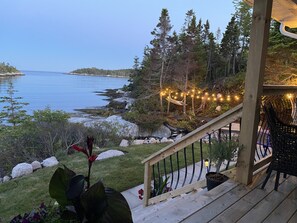 A wooden deck with a railing overlooking a body of water, surrounded by trees and a rocky shoreline.