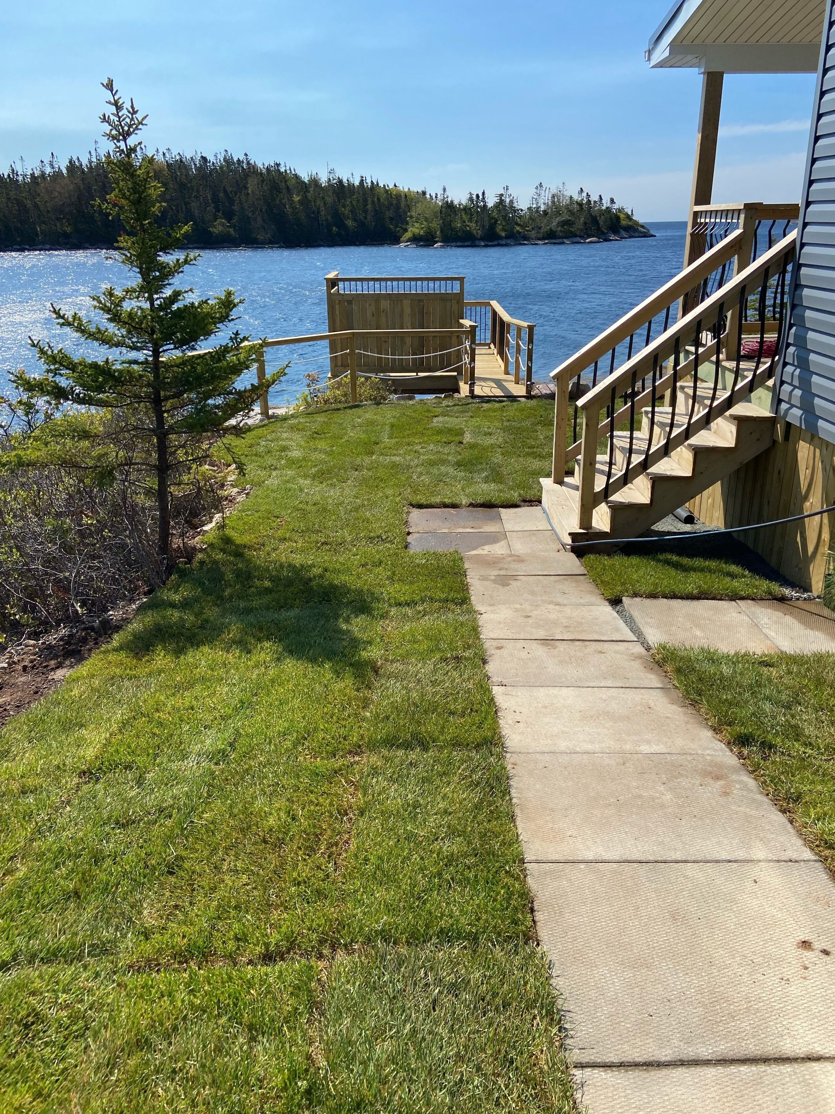 A wooden deck leading to a dock, a grassy area, and a view of a lake with a forested island in the distance.