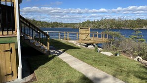 Une terrasse en bois avec un escalier menant à une plateforme d’observation surplombant un lac, le tout entouré d’une pelouse bien entretenue et d’un bâtiment en bois.