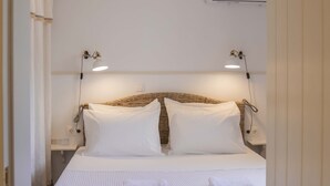 Un letto rifatto con lenzuola bianche e due cuscini, un comodino con una lampada e un condizionatore d'aria fissato al muro.