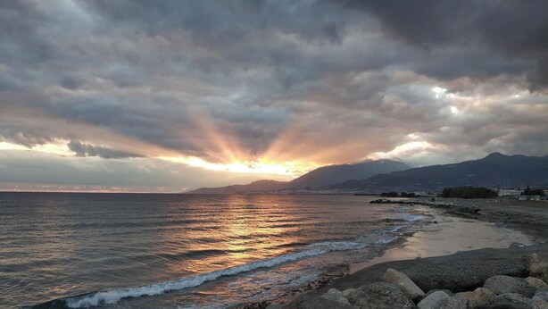 Una spiaggia con uno sfondo roccioso e un tramonto sull'oceano.