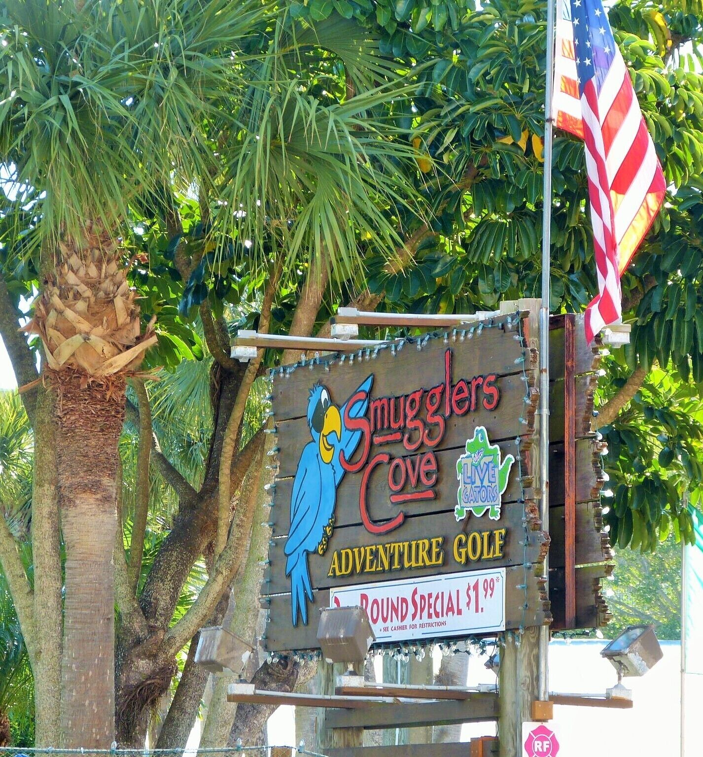 A sign for 'Smugglers Cove Adventure Golf' with a parrot illustration and a 'Round Special' price of $1.99.
