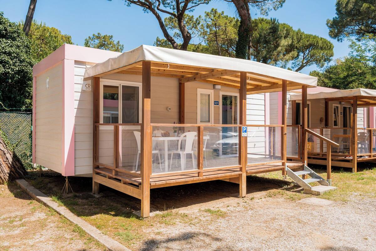 Ein kleines, eingeschossiges Mobilheim mit überdachter Veranda, einer Schiebetür und einem sichtbaren Sitzbereich im Freien.