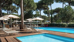 Zona de piscina con sillones y sombrillas, rodeada de árboles.