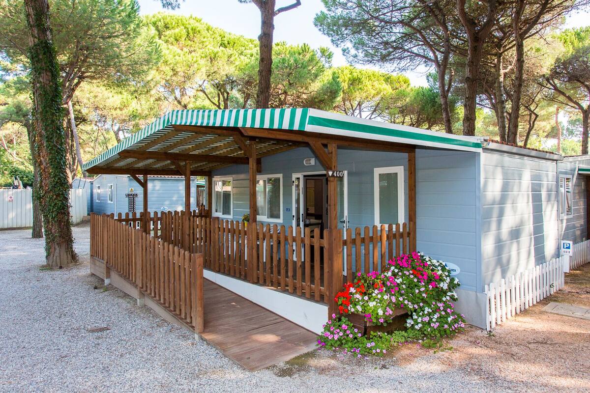 Ein kleines, eingeschossiges Mobilheim mit einer Holzdielen-Terrasse und einer überdachten Veranda.