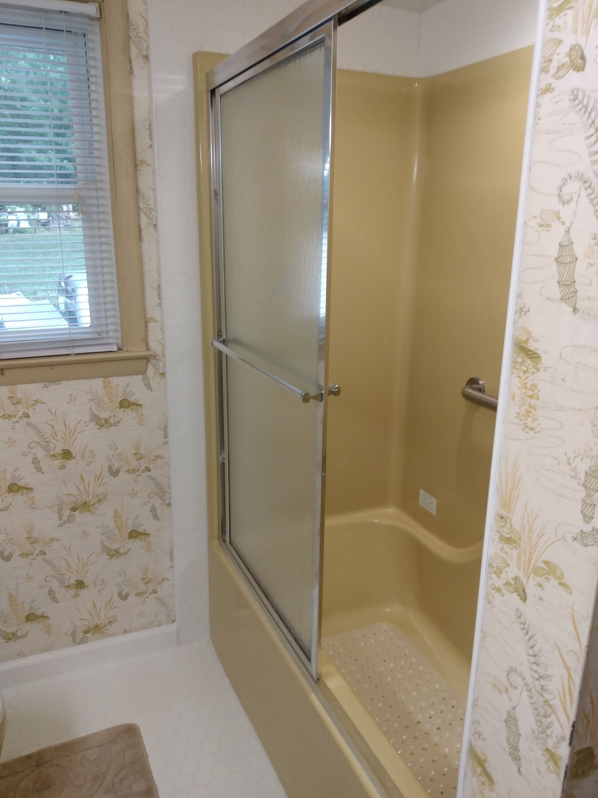 A bathroom with a shower, a toilet, and a window with blinds.