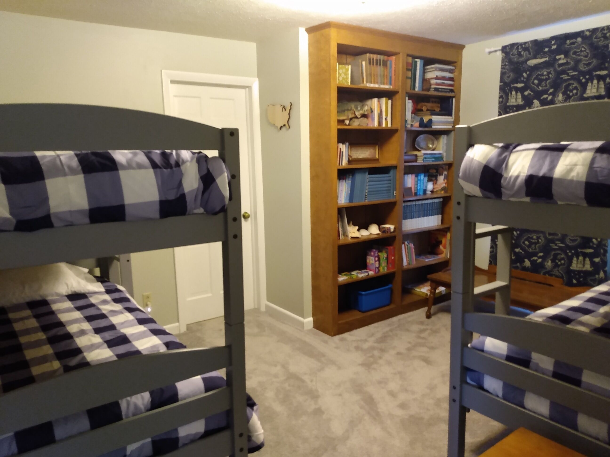 A room with bunk beds, a bookshelf, and a door.