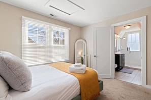 A bedroom with a bed, a window with blinds, a bathroom visible through an open door, and a mirror. - Stunning Nashville Charm - Convenient to Downtown (Nashville)