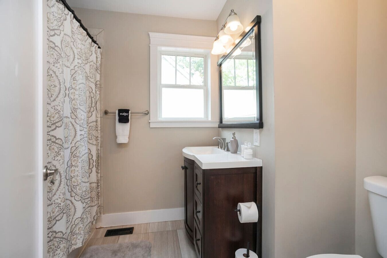 A bathroom with a shower, a toilet, a sink with a mirror, and a window.