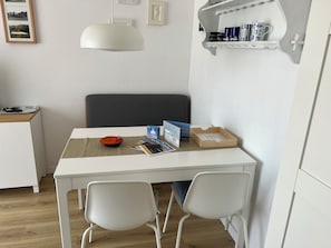 A small, white dining area with a table, two white chairs, a red bowl, a magazine, and a wooden box. - Lüttjer Kiwitt - perfect location for short distances and relaxing days (Wangerooge)